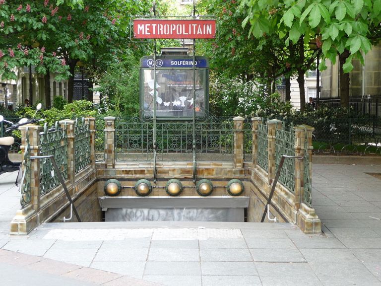 The entrance to Solférino station. Decorative metalwork and ceramic tiling are the key elements (the Metropolitain sign is a later addition; originally a "Nord-Sud" sign would have been installed. By Alex McLeod (originally posted to Flickr as P1000632.JPG) [CC-BY-SA-2.0], via Wikimedia Commons